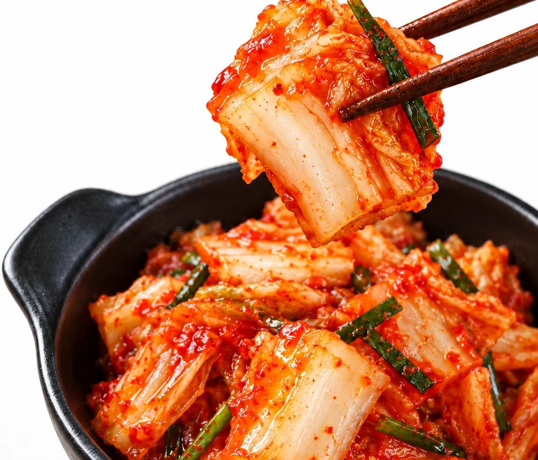 A piece of seasoned napa cabbage held above a bowl of kimchi, showing its white rib and layered leaf